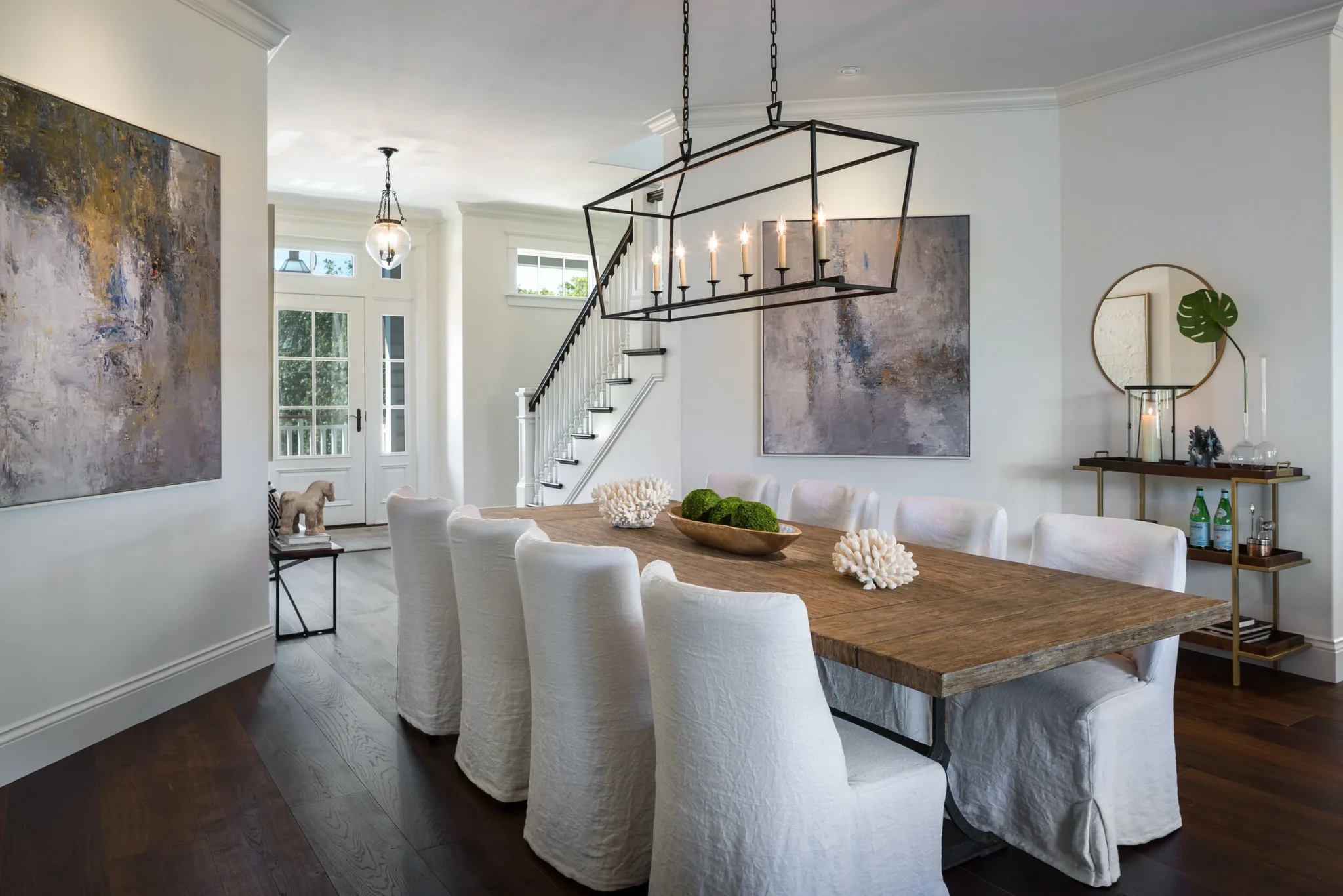 Modern dining room with a large wooden table surrounded by white slipcovered chairs, a black framed chandelier with candles overhead