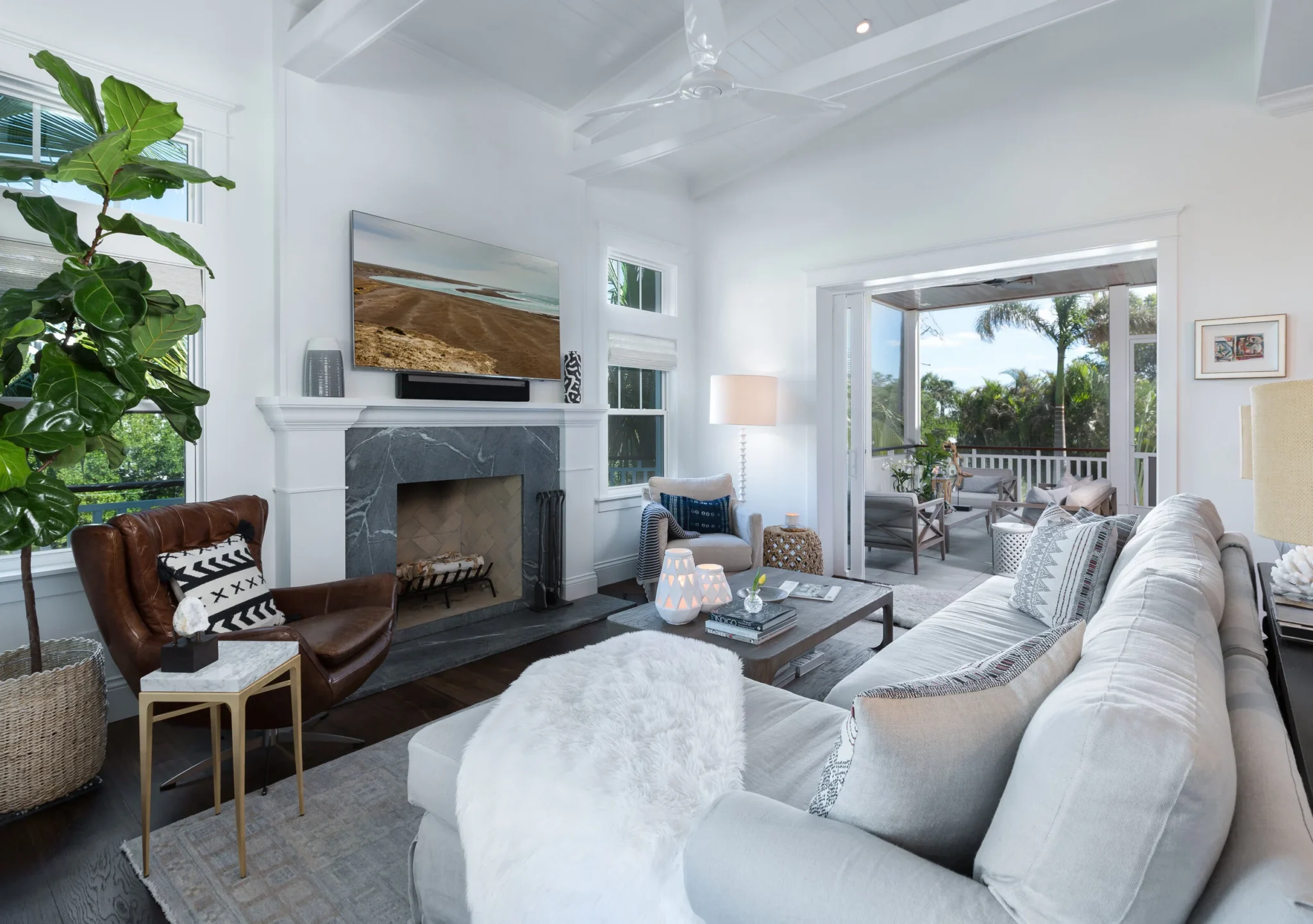 Living room with white walls, a fireplace, a flat-screen TV, a large window, and patio view, furnished with a white sofa, armchair, coffee table