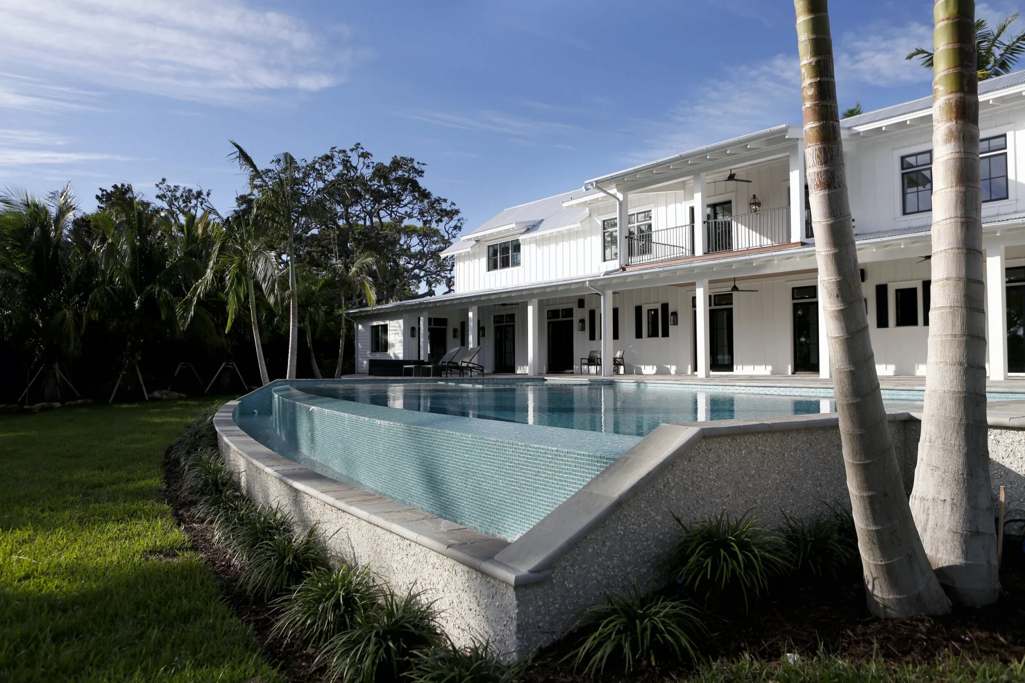 A modern two-story white house with a wrap-around porch and black railings, overlooking a backyard with a swimming pool, green grass