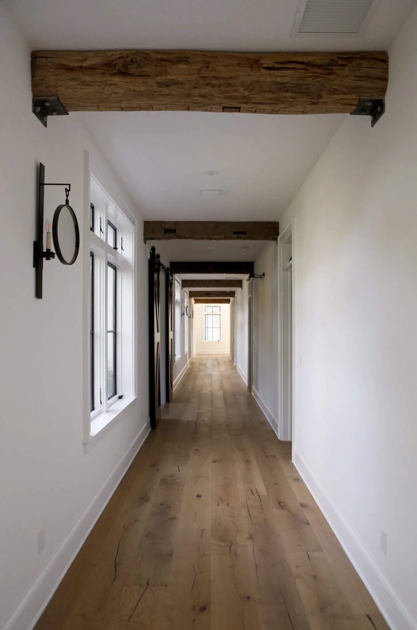 Long hallway in a modern house with white walls, wooden floors, and exposed wooden beams on the ceiling