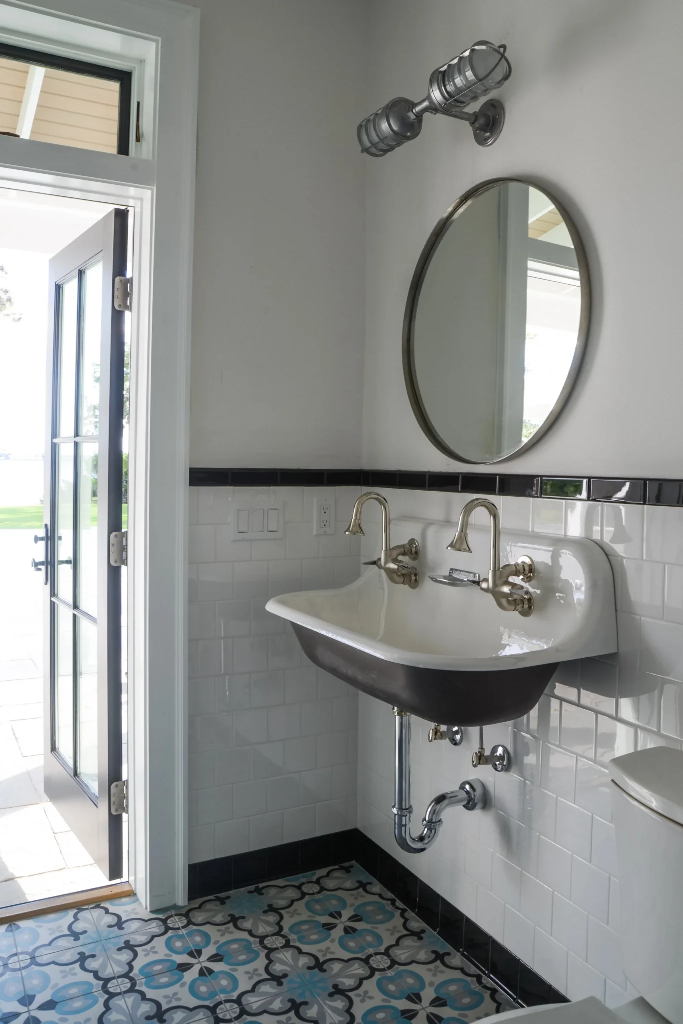 A bathroom with a black and white tile floor, a white sink with vintage-style brass faucets, an oval mirror