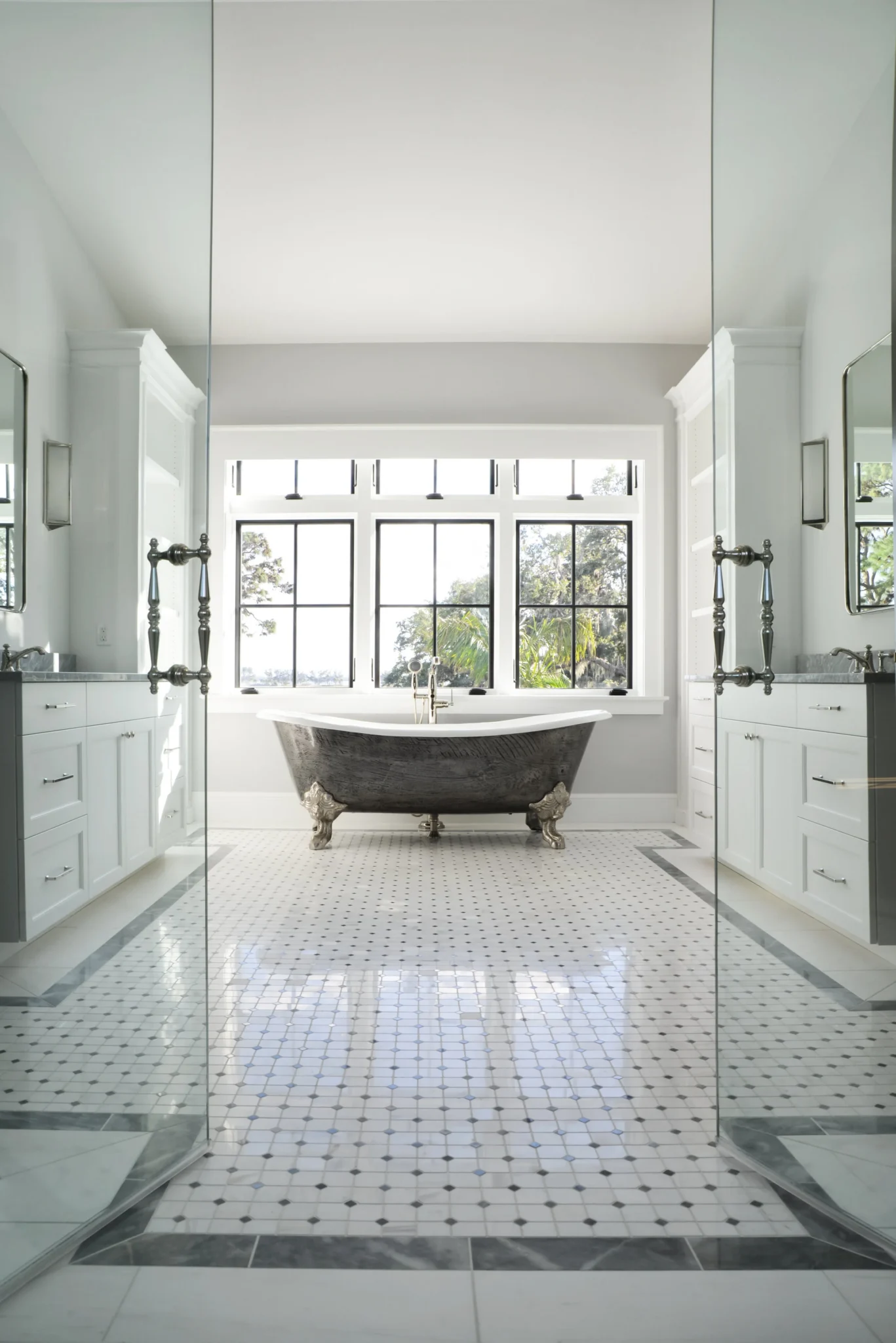 A bathroom featuring a black clawfoot bathtub with ornate silver feet, situated in front of large windows with a view of greenery outside