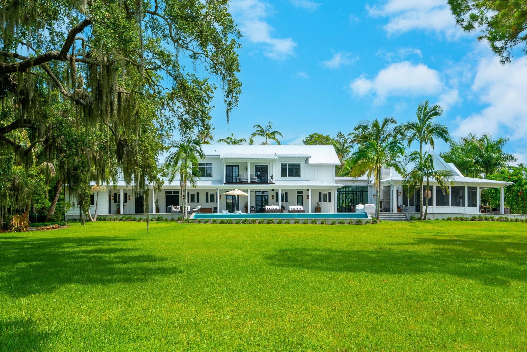 White two-story modern farmhouse with a long pool terrace, seen across the lawn