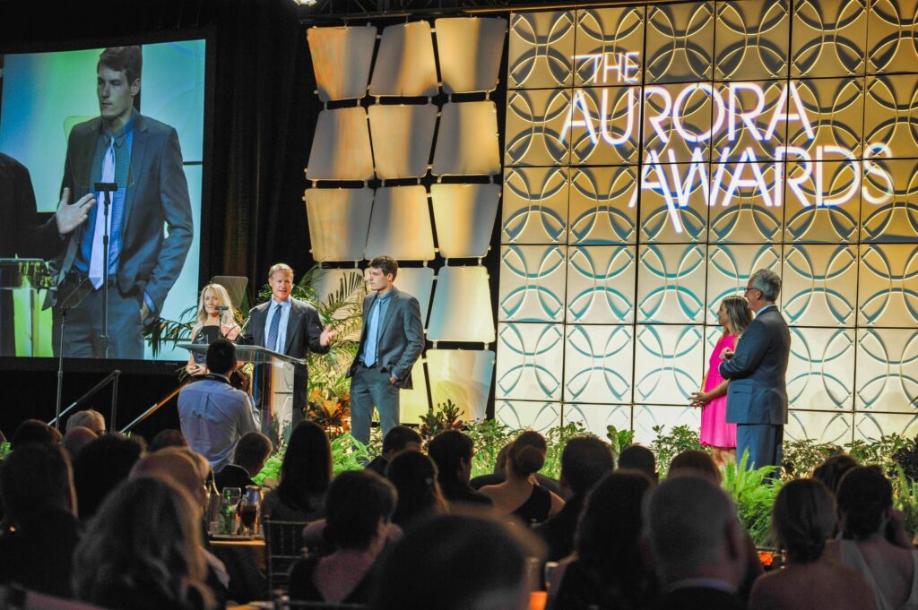 Greg Ross at the podium accepting Ross Built’s first Aurora Award, with Lee and Andrew Ross beside him, 2019