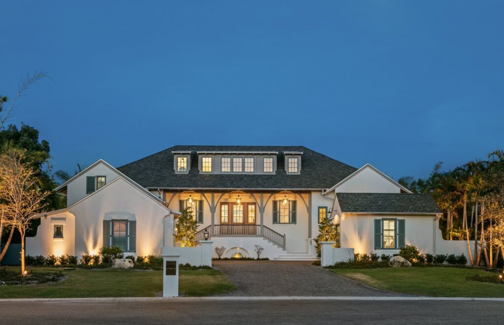 White stucco home at dusk with lit porch and dormers, the new home Ross Built built for its first client, 2021