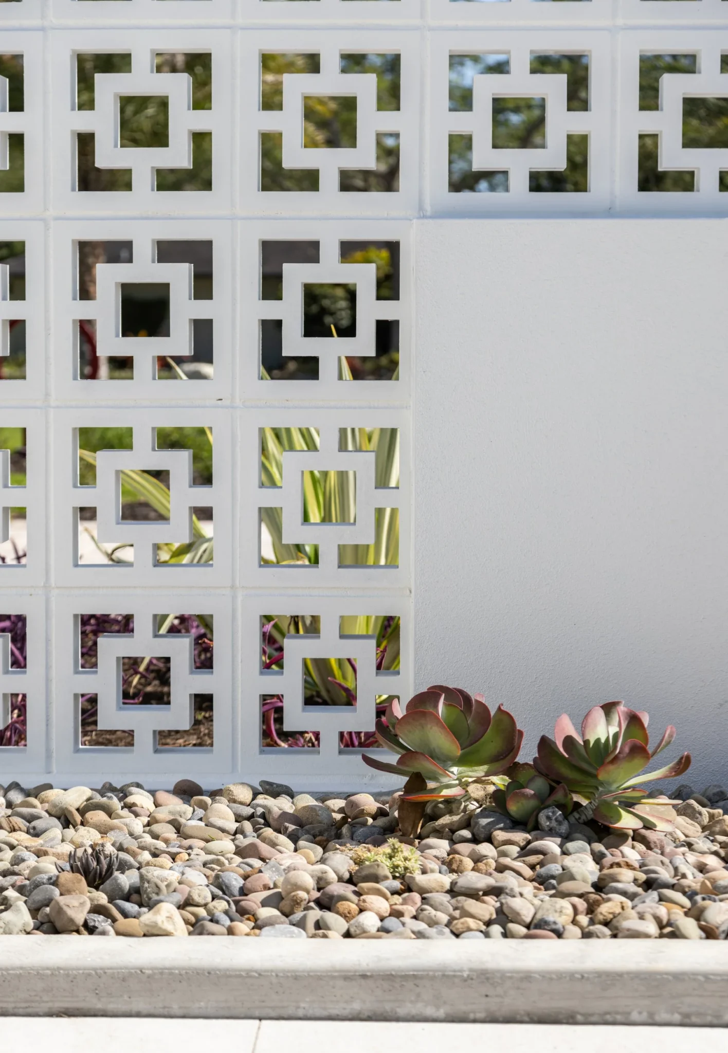Decorative white wall with geometric cutouts, landscaping rocks, and succulents in front