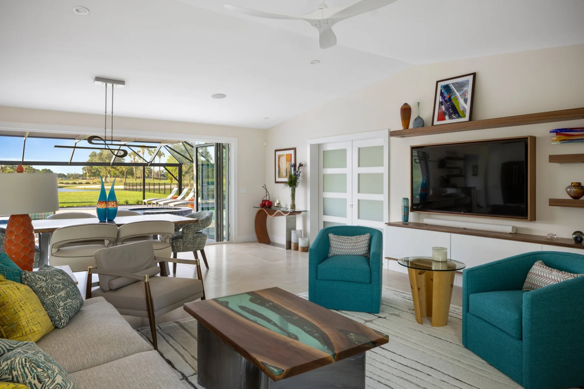 Bright living room with teal armchairs, a beige sofa, a wooden coffee table, and a view of the outdoor patio through sliding glass doors