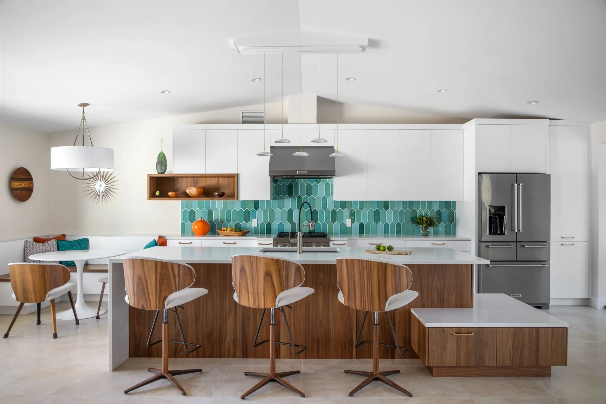 Modern kitchen with a white countertop island, wooden bar stools, teal tile backsplash, stainless steel appliances