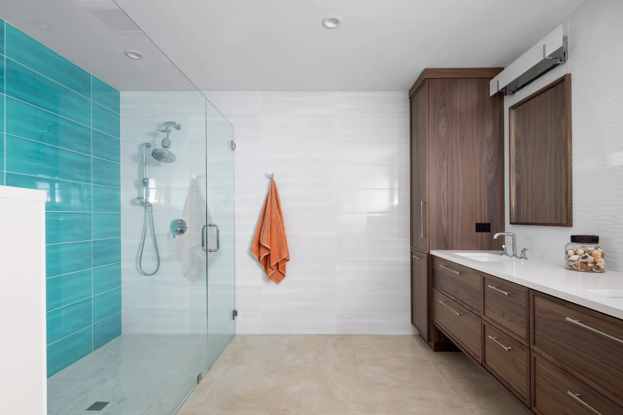 Modern bathroom with a walk-in glass shower on the left, an orange towel hanging on the wall, and wooden cabinets with a mirror and sink on the right