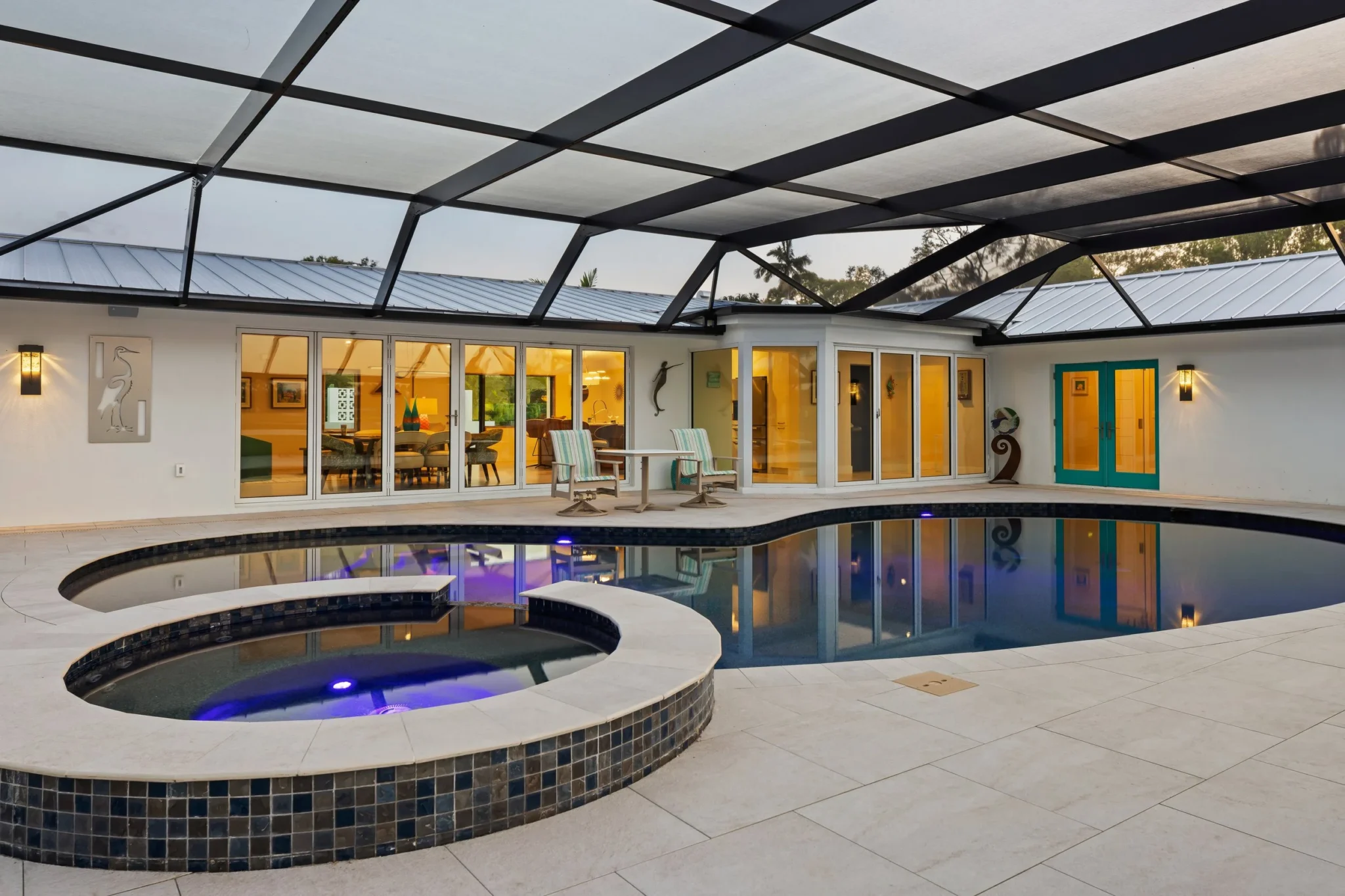 Exterior view of a house with a swimming pool and hot tub, enclosed by a screened patio with glass sliding doors, outdoor chairs