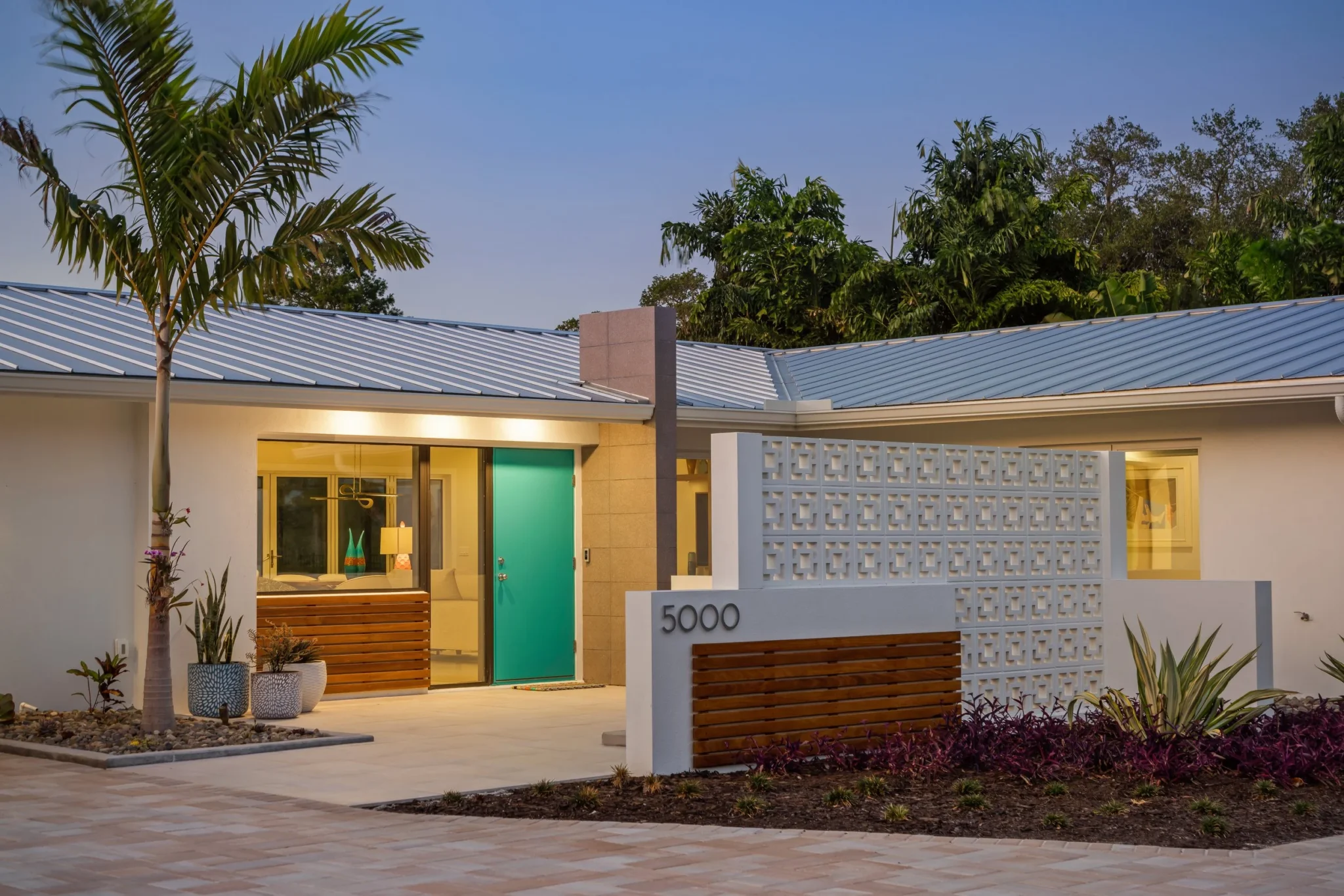 Modern house with a white exterior, teal front door, and a brick and white lattice wall