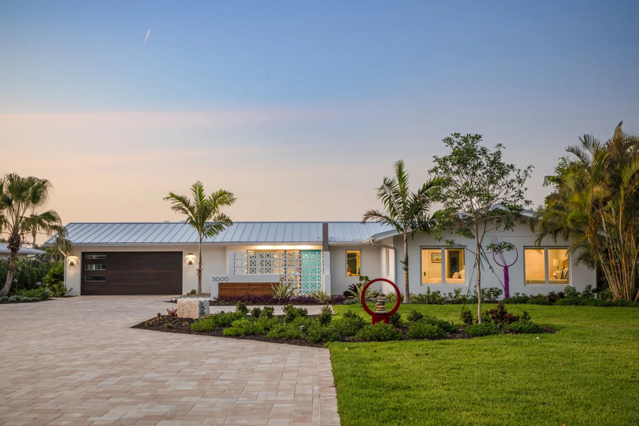 A modern single-story house with a well-maintained front yard, palm trees, a paved driveway
