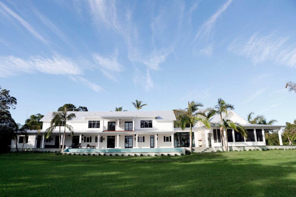 White board-and-batten home on Palma Sola Bay with a long pool and wide lawn, designed by Sweet Sparkman Architecture and Interiors and built by Ross Built, 2017